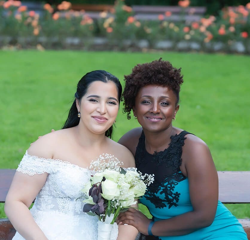 Two women sitting on a bench in front of some flowers.