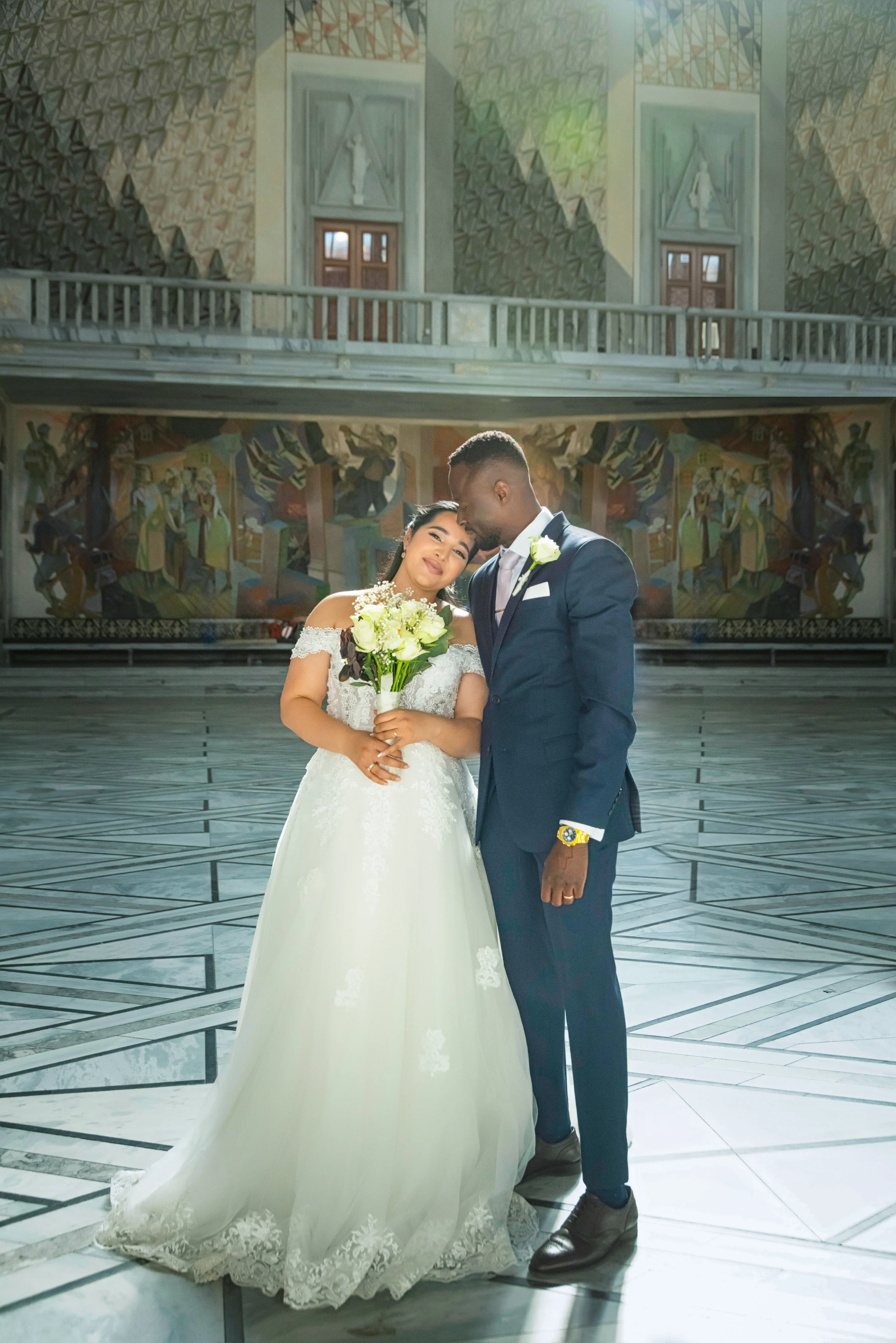 A bride and groom pose for the camera in front of a mural.