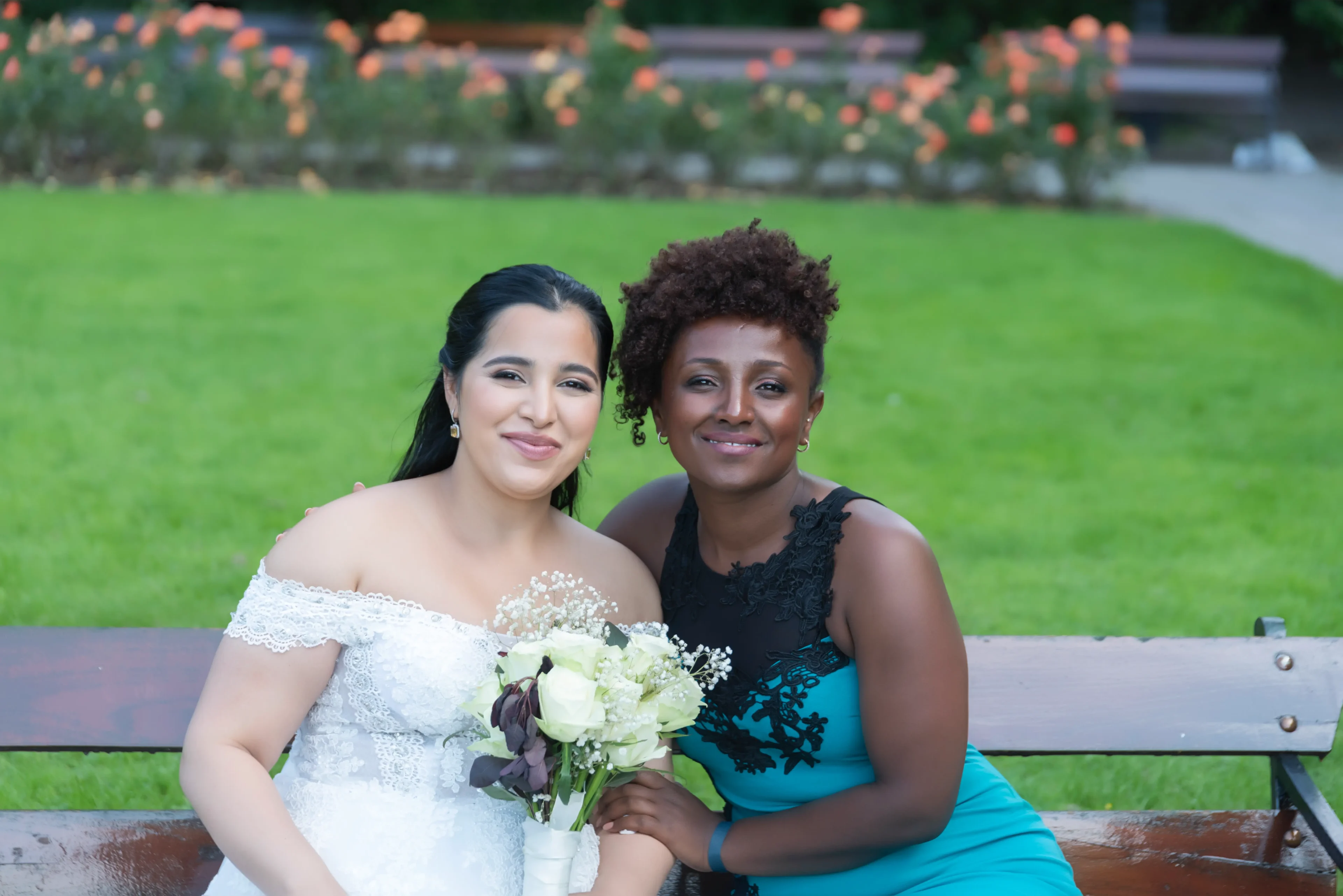 Two women posing for a picture in front of some flowers.